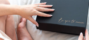 Woman on bed opening a Blum Organics Blum Mama Gift box package